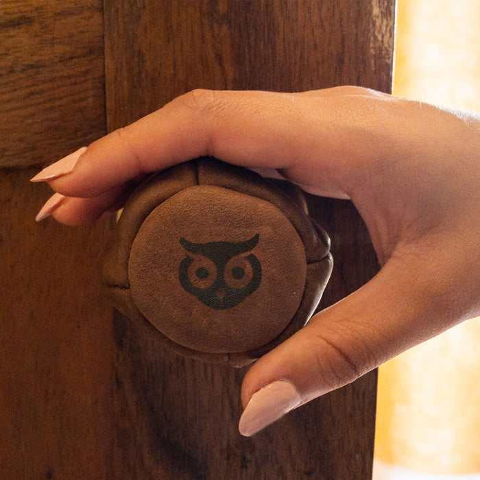Hide & Drink's Door Knob Cover being held, displaying its practical and stylish design. Made from fine Full Grain Leather, this baby proof door knob cover is part of a small batch production, showcasing handmade quality and artisan craftsmanship from La Antigua Guatemala.