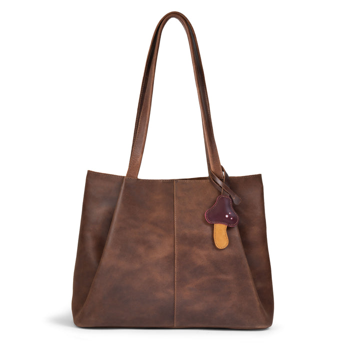 Hide & Drink Bag Charms attached to a trendy brown handbag, showcasing a pineapple design perfect for personalization. This purse charm for tote & backpacks made from premium full grain leather reflects StockyardX's commitment to small batch production. Each piece highlights hand cut, hand sewn craftsmanship along with fire branding, handmade in La Antigua Guatemala & Oaxaca Mexico.
