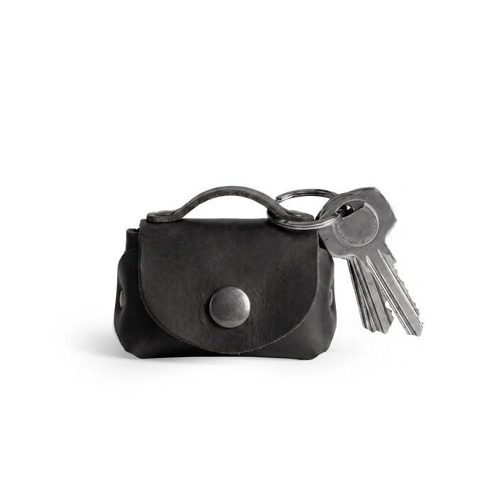 A stylish Tiny Handbag Keychain in black leather by Hide & Drink, featuring a key ring holder. This functional piece is made from high-quality Full Grain Leather and emphasizes small batch production and meticulous artisan craftsmanship.